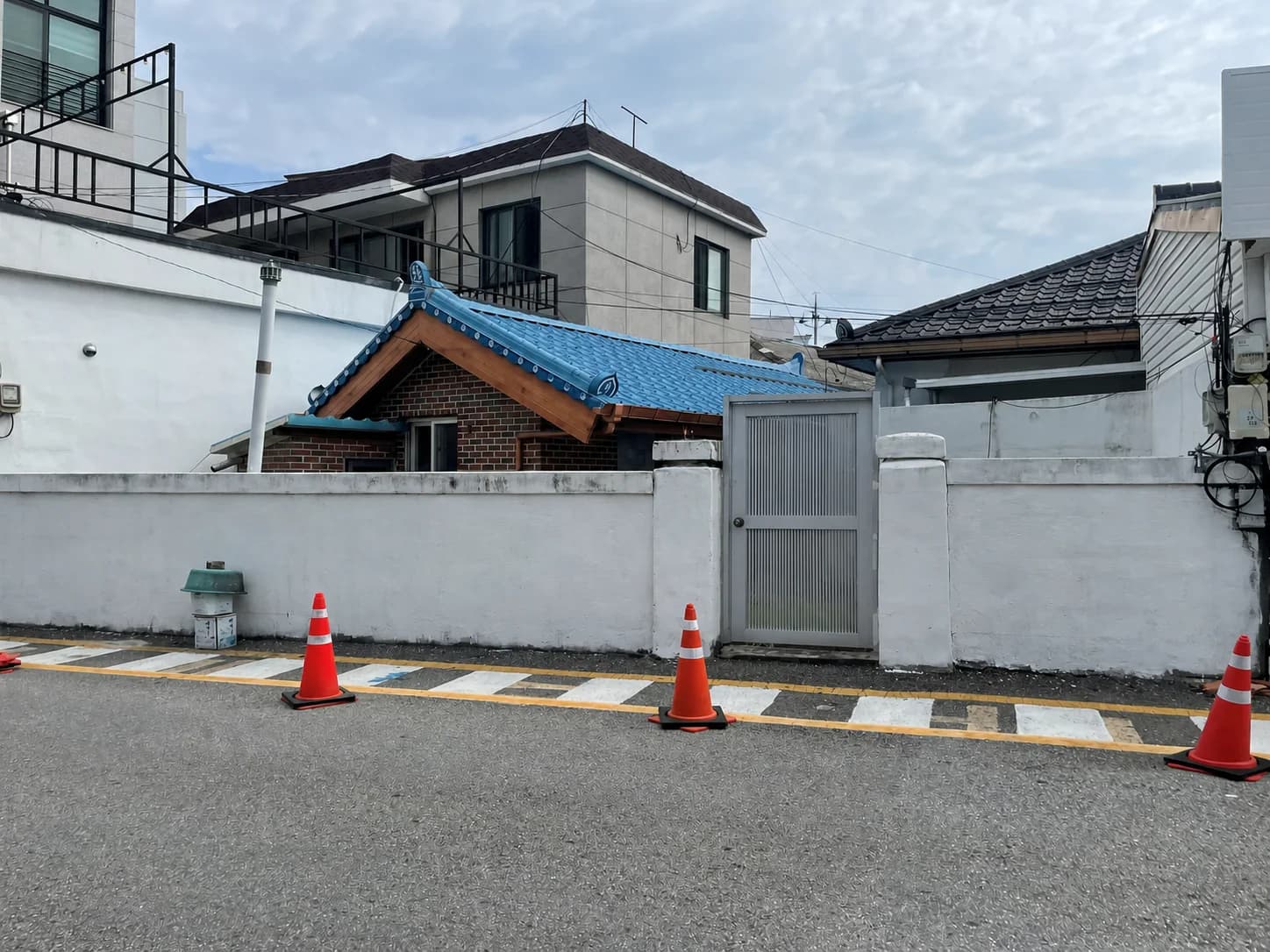 담장 너머 파란 기와지붕이 보이는 작은 단독주택 외관