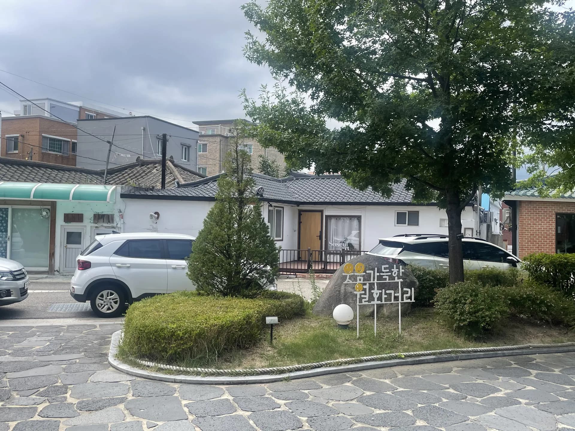 큰 나무와 낮은 지붕 건물이 보이는 마당 입구